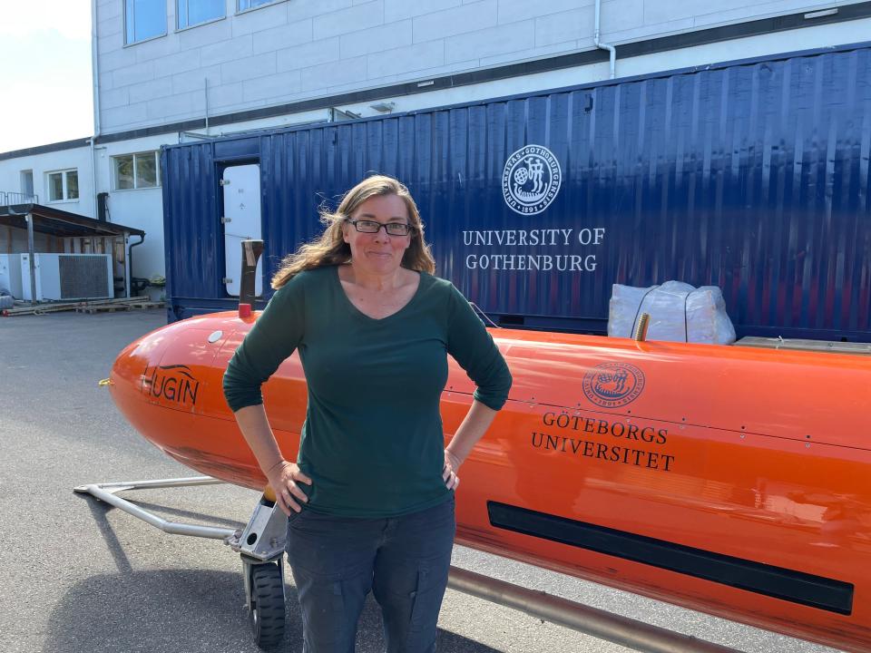 A woman in a green shirt smiles at the camera while standing in front of the red Ran science submersible.