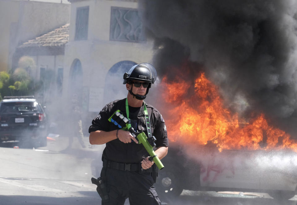 A police officer stands guard while a police vehicle burns during a protest over the death of George Floyd in Los Angeles, Saturday, May 30, 2020. Protests across the country have escalated over the death of George Floyd who died after being restrained by Minneapolis police officers on Memorial Day, May 25.(AP Photo/Ringo H.W. Chiu)