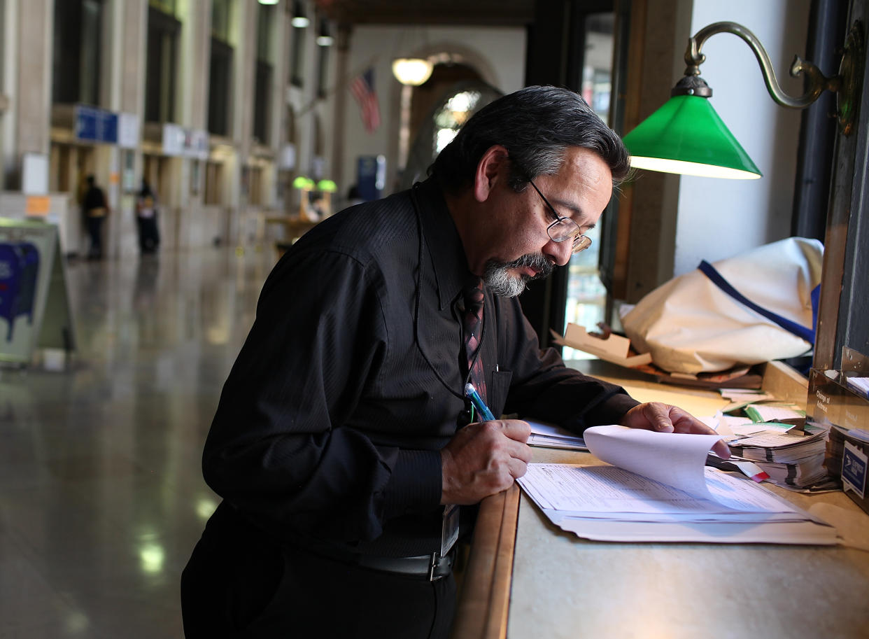 A U.S. Postal Service customer Ricardo Romero signs his tax forms before mailing them at the James A. Farley Post Office in New York City. (Photo by Justin Sullivan/Getty Images)