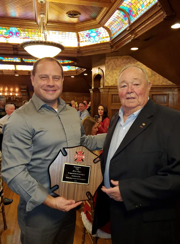 From left, Boardman Fire Chief Mark Pitzer accepts plaque from retired Sebring Fire Chief Jim Cannell at the annual Mahoning County Fire Chief Association holiday dinner in 2019. Cannell died July 23, 2022.