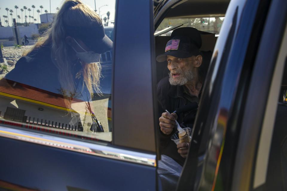 A woman in a visor talks to a man sitting in a vehicle.