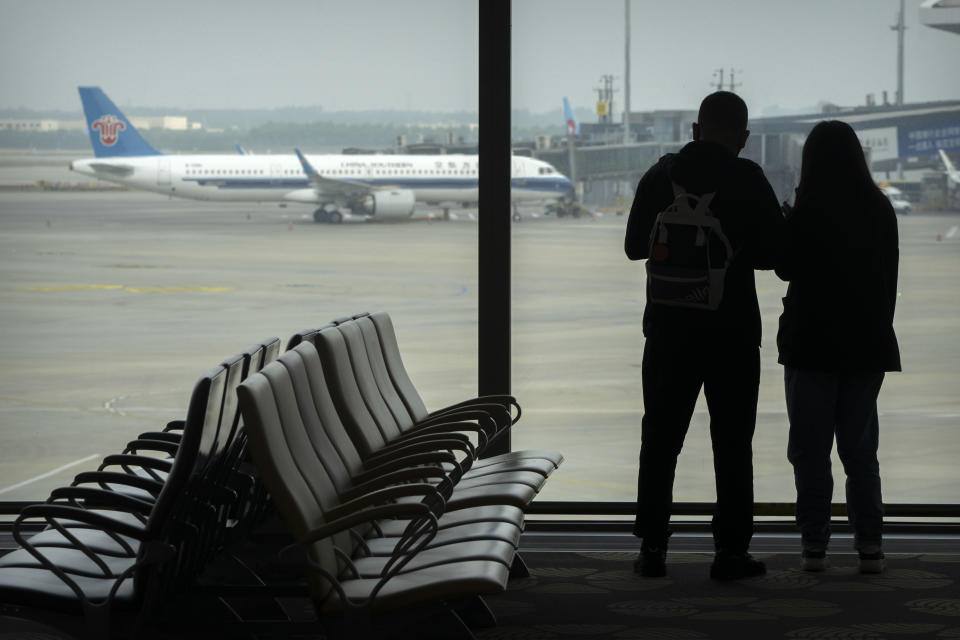 Travelers stand at a window with a parked jetliner from China Southern in the background, at Beijing Daxing International Airport, in Beijing, Sunday, May 28, 2023. China's first domestically made passenger jet flew its maiden commercial flight on Sunday, as China looks to compete with industry giants such as Boeing and Airbus in the global aircraft market. (AP Photo/Mark Schiefelbein)