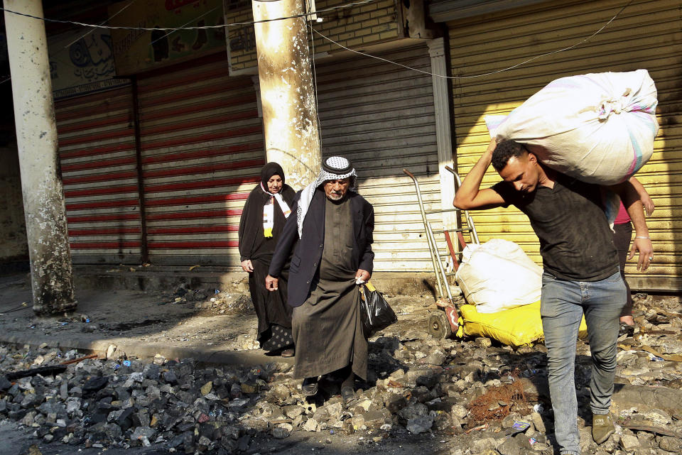 Civilians pass while anti-government protesters clean Rasheed street that was damaged in clashes between security forces and anti-government protesters, in Baghdad, Iraq, Sunday, Dec. 1, 2019. Iraq's parliament approved the resignation of Prime Minister Adel Abdul-Mahdi on Sunday, amid ongoing violence and anti-government demonstrations in the capital. (AP Photo/Hadi Mizban)