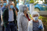 People wearing a face masks for protection against the COVID-19 infection, wait in line to have their temperature checked before being allowed in a voting station in Bucharest, Romania, Sunday, Sept. 27, 2020. Some 19 million registered voters are choosing local officials, council presidents and mayors to fill more than 43,000 positions across the European Union nation. ( AP Photo/Vadim Ghirda)