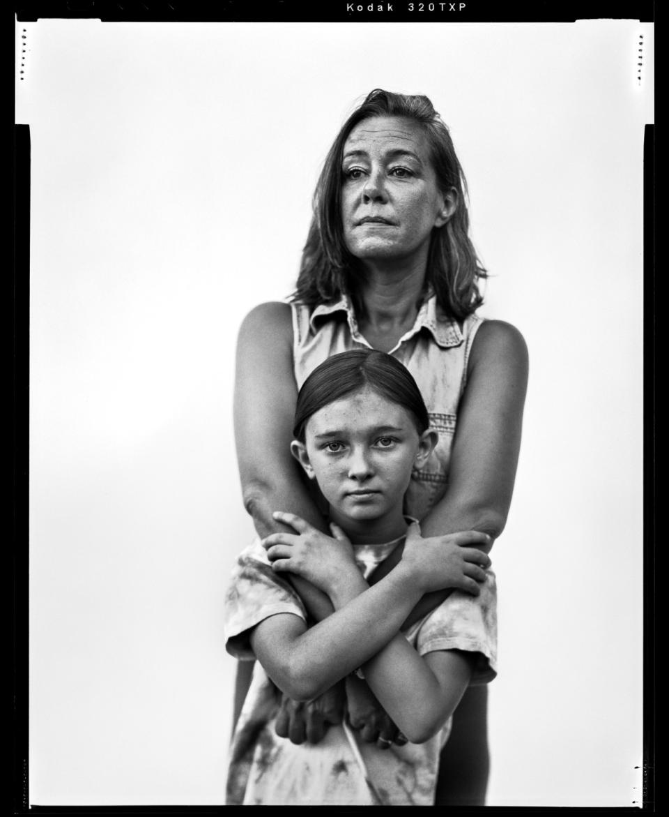 Black and white film photo of a woman, Jamie Eagan, with her 8-year-old daughter behind her with her arms around her