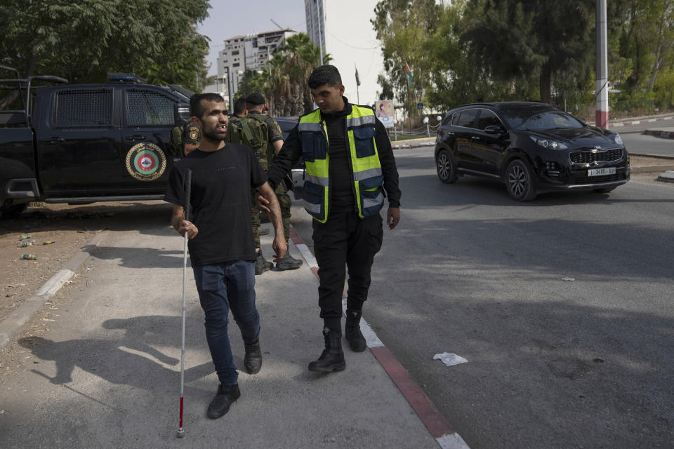 A Palestinian police officer helps a blind man cross the street as newly deployed security forces stand guard at a main junction in the occupied West Bank city of Jenin, Sunday, Aug. 13, 2023. (AP Photo/Nasser Nasser)