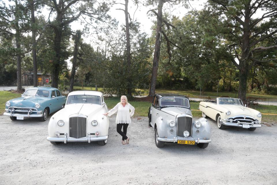 Sherri Anderson stands among 4 of the 7 classic cars that she and her husband, Bill own. The cars included in the photo are a 1951 Ford Deluxe, a 1956 Bentley S1, a 1952 Bentley R type, and a 1953 Packard convertible.