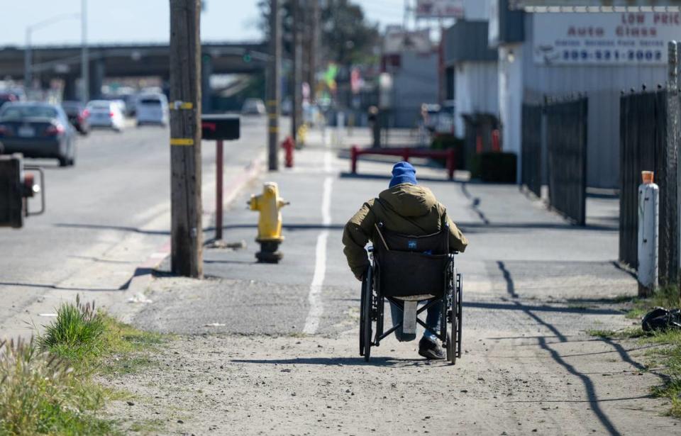 Un hombre en silla de ruedas se desplaza por una acera de tierra y grava en South Ninth Street en Modesto, California, el sábado 16 de marzo de 2024.