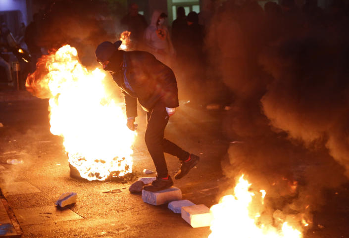 An anti-government protester passes between burning tires during ongoing protests against the country's financial woes, in Beirut, Lebanon, Wednesday, Jan. 15, 2020. Lebanese security forces arrested 59 people, the police said Wednesday, following clashes overnight outside the central bank as angry protesters vented their fury against the country's ruling elite and the worsening financial crisis. (AP Photo/Hussein Malla)