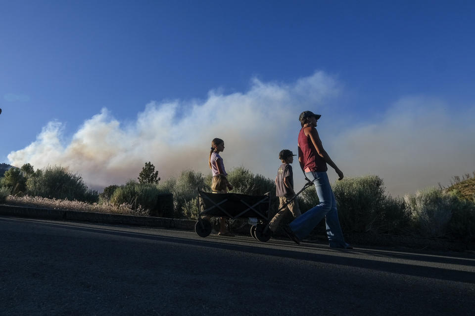 Residents walk by as smoke rises from the Sheep Fire burning in Wrightwood, Calif., Sunday, June 12, 2022. (AP Photo/Ringo H.W. Chiu)