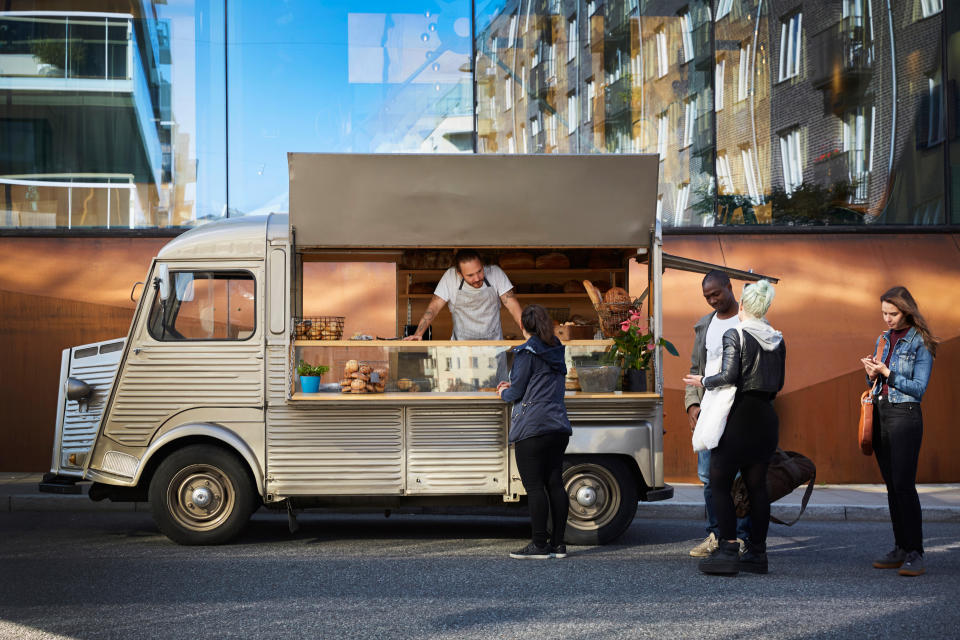 Multi-ethnic customers buying from owner in food truck against building