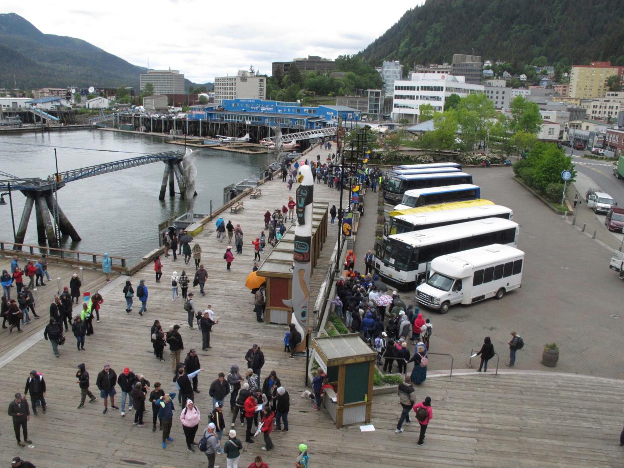 People mill about on the sea walk along which cruise ships dock on June 12, 2023, in downtown Juneau, Alaska. Buses stand ready to take tourists to activities around town.