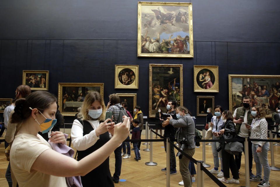 People take snapshots as they visit the Louvre museum, Wednesday, May, 19, 2021 in Paris. Museums must restrict entries so there is 8 square meters of space (86 square feet) per visitor. Café and restaurant terraces are reopening Wednesday after a shutdown of more than six months deprived people of what feels like the essence of life — sipping coffee and wine with friends outdoors — to save lives during the coronavirus pandemic. (AP Photo/Thibault Camus)