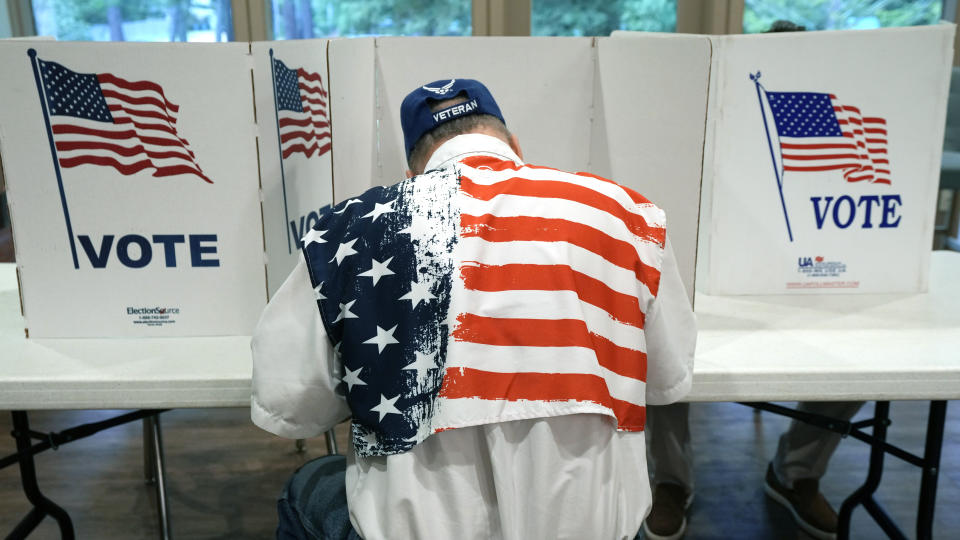 A patriotic voter sits at a voting kiosk and selects his choices in a party primary in Jackson, Miss., Tuesday, Aug. 8, 2023. Voters are casting their ballots in party primaries in a number of county and statewide elected offices. (AP Photo/Rogelio V. Solis)