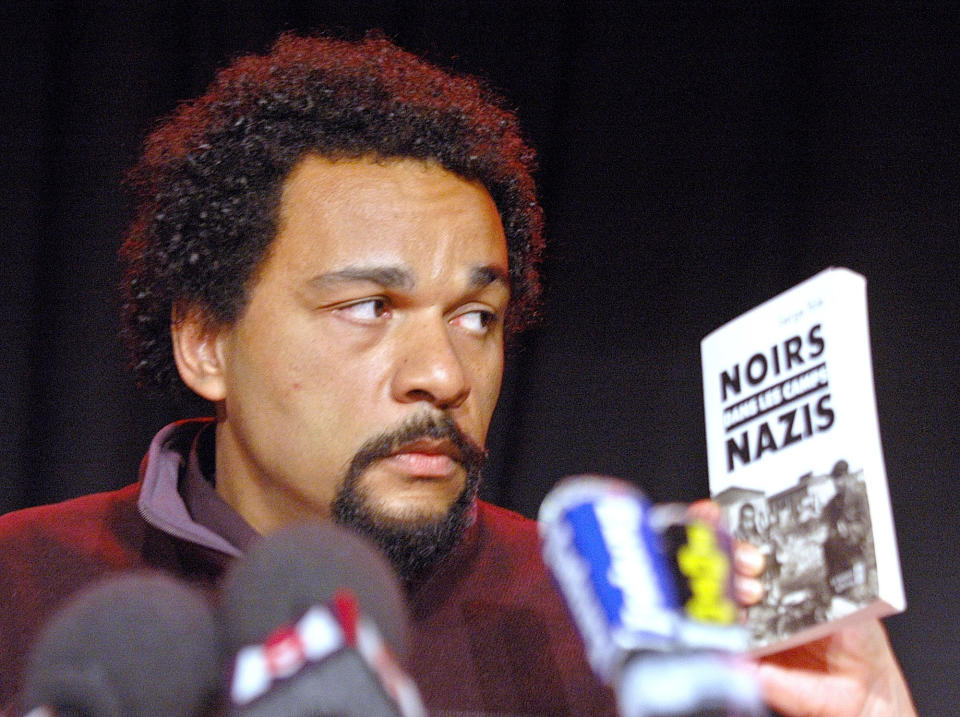 FILE - In this Feb. 19, 2005 file photo, French comic Dieudonne M'Bala M'Bala looks at a book "Blacks in the Nazi camps" by Serge Bile during a statement at La Main d'Or theater, in Paris. The Paris prosecutor's office said Thursday Jan 2, 2013, it is investigating threats against a comedian the French interior minister wants banned from the stage for what he says are racist and anti-Semitic performances. (AP Photo/Jacques Brinon, File)