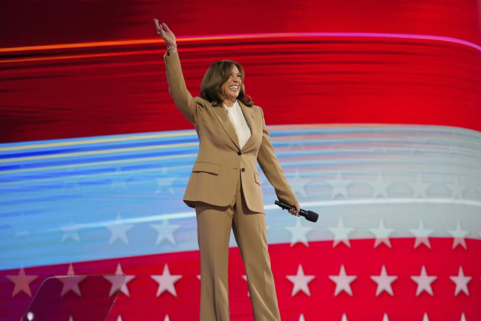 Vice President Kamala Harris, dressed in a fully tanned suit, waves on stage at the Democratic National Convention.