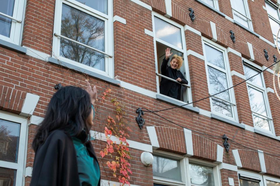 woman in apartment waving down to friend on street