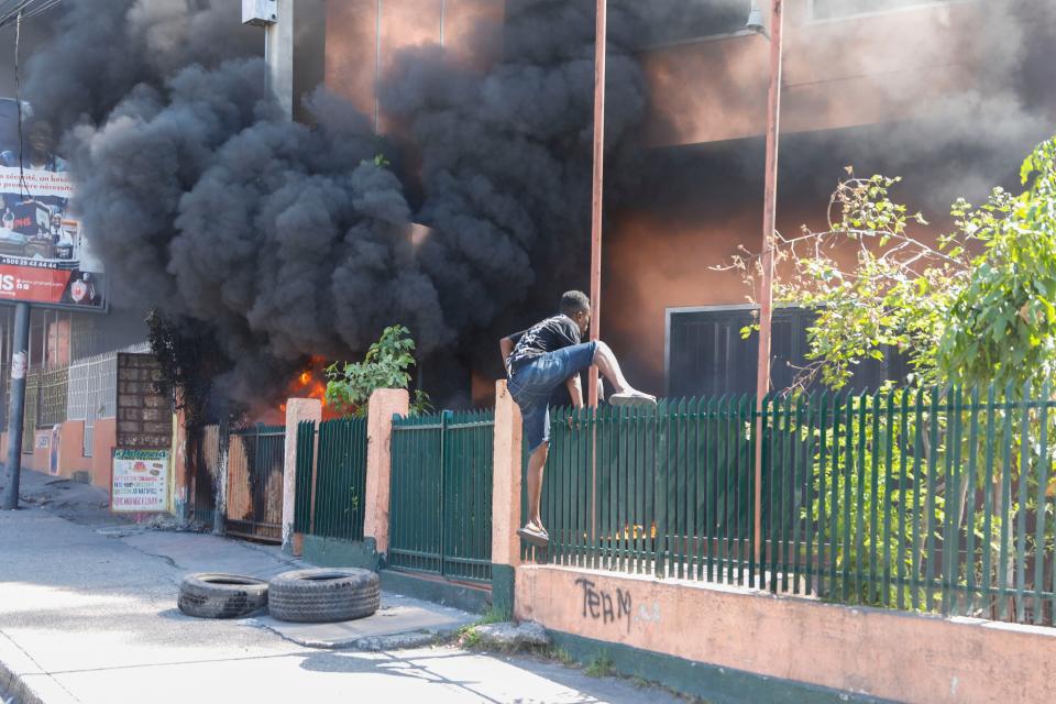 A man climbs the fence of an office of Haiti's power company set on fire during a protest to demand the resignation of the Prime Minister Ariel Henry in Port-au-Prince, Haiti, Friday, March 1, 2024. (AP Photo/Odelyn Joseph)