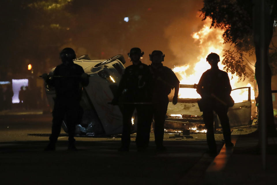 Police stand near a overturned vehicle and a fire as demonstrators protest the death of George Floyd, Sunday, May 31, 2020, near the White House in Washington. Floyd died after being restrained by Minneapolis police officers (AP Photo/Alex Brandon)