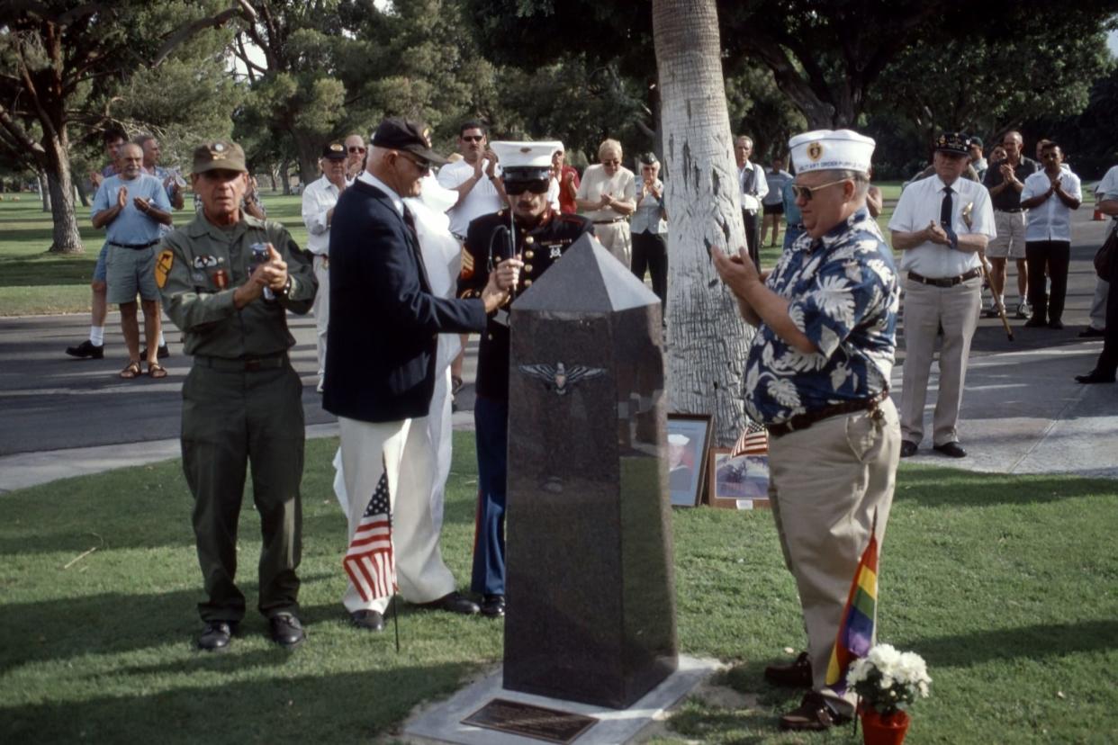 LGBT Veterans Memorial, Cathedral City, California with several miltary LGBT veterans surrounding the monument and people in the background clapping on a sunny day