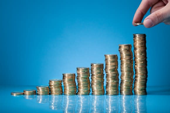 A hand placing a coin on stacks of coins.