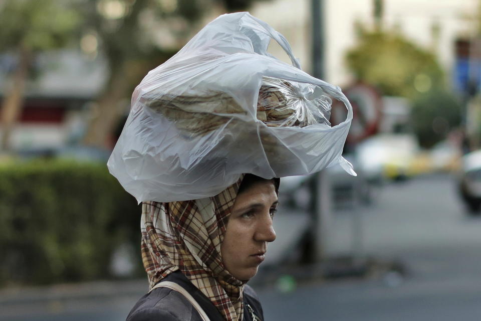 FILE - In this July 24, 2019 file photo, a woman carries bread on her head while she crosses a street in the Syrian capital, Damascus. Exchange rate distortions in war-torn Syria have allowed the government of Bashar Assad in Damascus to divert at least $100 millions of international aid to its coffers, according to new research. (AP Photo/Hassan Ammar, File)