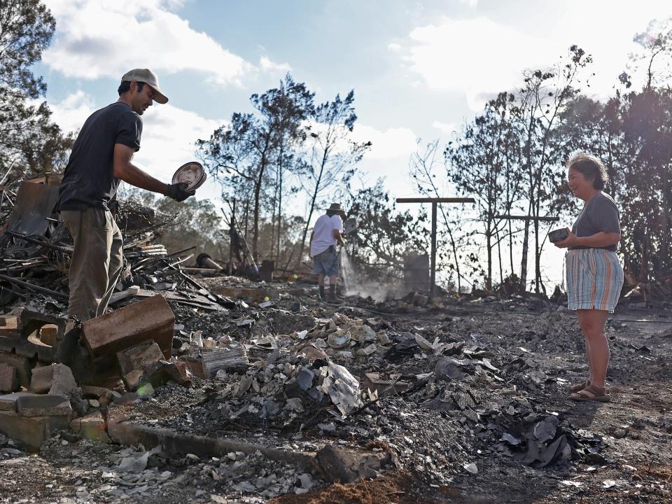 Brook Cretton (L) holds a stack of dishes that he salvaged from the rubble of a home that was destroyed by wildfire on August 12, 2023 in Kula, Hawaii.