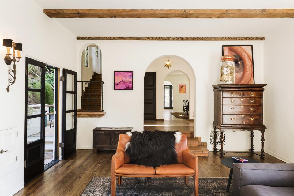 A Juliet balcony adds charm to the stairwell and a vintage '70s C-print rests atop a 17th-century chest on stand. They found the vintage <a rel="nofollow noopener" href="https://www.cassina.com/en/designer/mario-bellini" target="_blank" data-ylk="slk:Mario Bellini for Cassina;elm:context_link;itc:0;sec:content-canvas" class="link ">Mario Bellini for Cassina</a> leather loveseat at a Pasadena antique store. “It was in a pile, with stuff on top of it and underneath it,” Aniello says. “We weren’t sure it was actually a signed piece. Then when we got in the car and saw it was a Cassina, we were like . . .” Downs says. “We got it for a fricking steal,” Aniello finishes. The painting next to the arched entryway is entitled "Pink Olana" by Daniel Heidkamp.