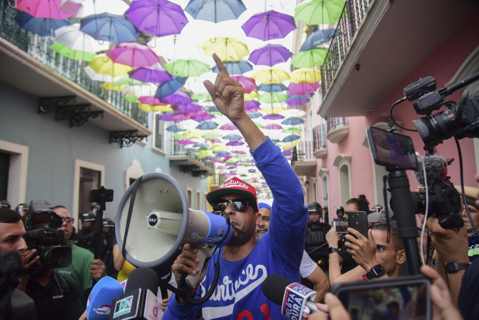 Activist Tito Roman speaks to protesters through a megaphone near La Fortaleza governor's residence in San Juan, Puerto Rico, Sunday, July 14, 2019. Protesters are demanding Gov. Ricardo Rosselló step down for his involvement in a private chat in which he used profanities to describe an ex-New York City councilwoman and a federal control board overseeing the island's finance. (AP Photo/Carlos Giusti)