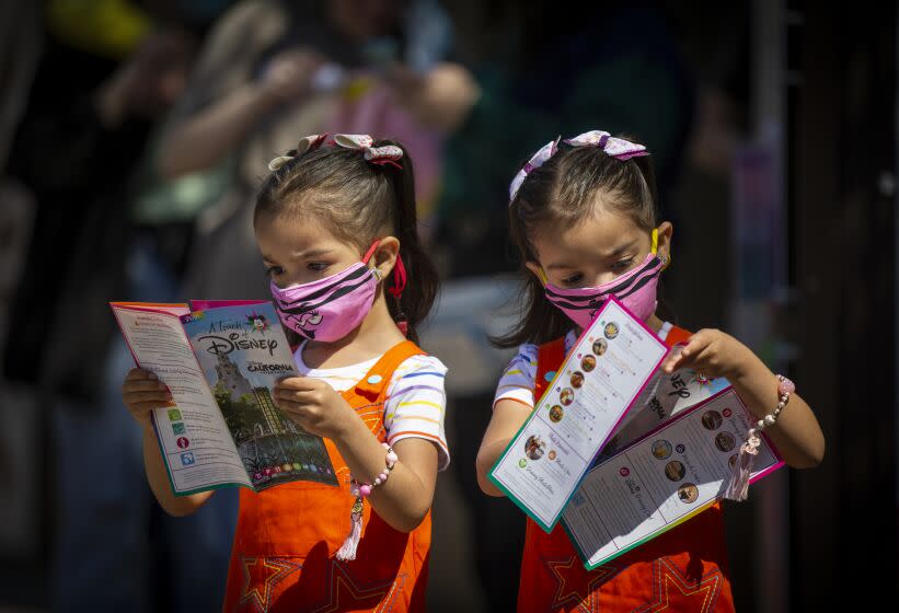 ANAHEIM, CA - March 18: Three-year-old twins Abigail Flores, left, and Aubrey Flores look at maps upon arrival of the debut of Disney California Adventure's "A Touch of Disney" food event at Disney California Adventure Park Thursday, March 18, 2021 in Anaheim, CA. This spans the entire DCA park and allows guests to eat, interact with characters and explore the grounds. A Touch of Disney, the new limited-time ticketed experience at Disney California Adventure Park which has sold out, takes place March 18 through April 19, 2021. (Allen J. Schaben / Los Angeles Times)