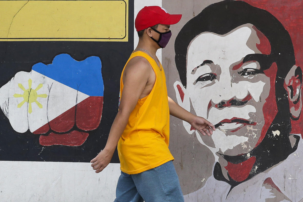 A man wearing a protective mask walks past an image of Philippine President Rodrigo Duterte in Manila, Philippines on Friday March 20, 2020. (AP Photo/Aaron Favila)