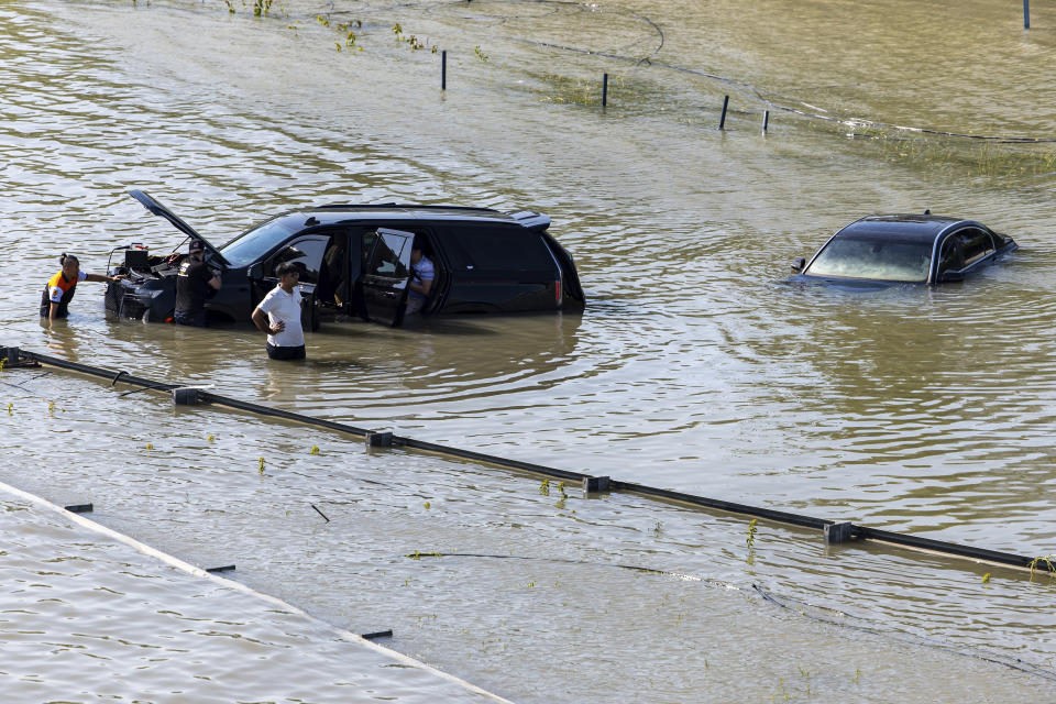 FILE - A group of people work to recover an abandoned vehicle taken by floodwater caused by heavy rain in Dubai, United Arab Emirates, April 18, 2024. A new report says climate change played a role in the floods. (AP Photo/Christopher Pike, File)