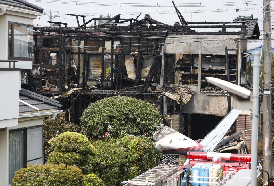The tail section of a crashed light plane and burning house are seen after the plane went down in a residential area and burst into flames, in Chofu, outskirt of Tokyo