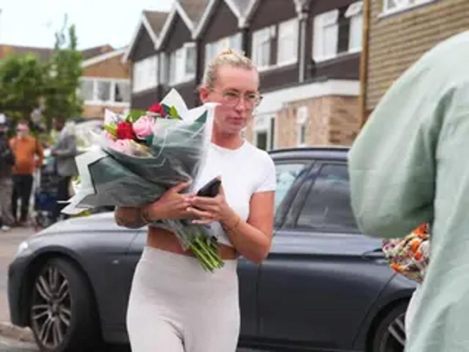 A woman delivers floral tributes near to the scene in Ashlyn Close, Bushey, Hertfordshire (PA)