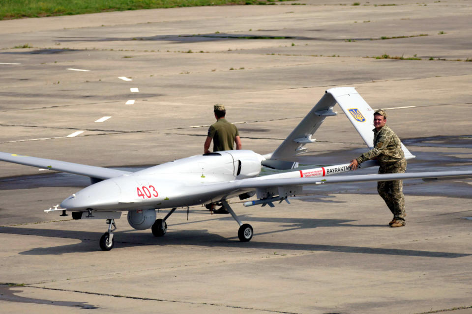 Servicemen push a large drone across a tarmac.