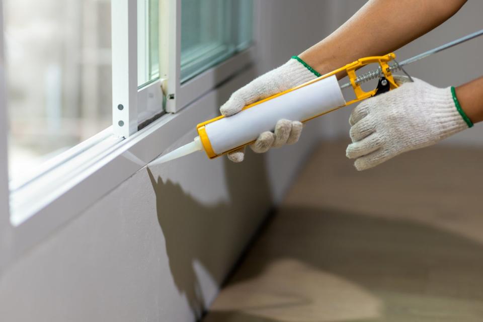 Gloved hands sealing a window frame with caulk 