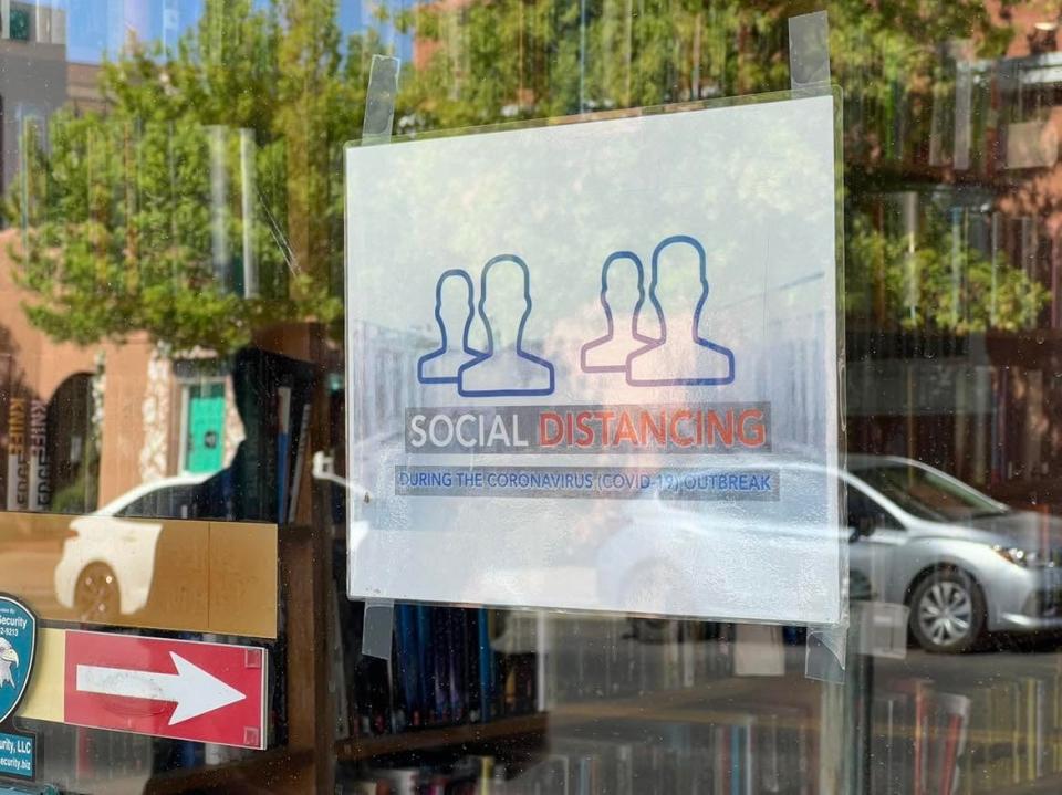 Downtown traffic is reflected in the window of COAS Books in Las Cruces, N.M., where a sign in the window requests customers maintain physical distance during the COVID-19 pandemic, on Thursday, April 28, 2022.