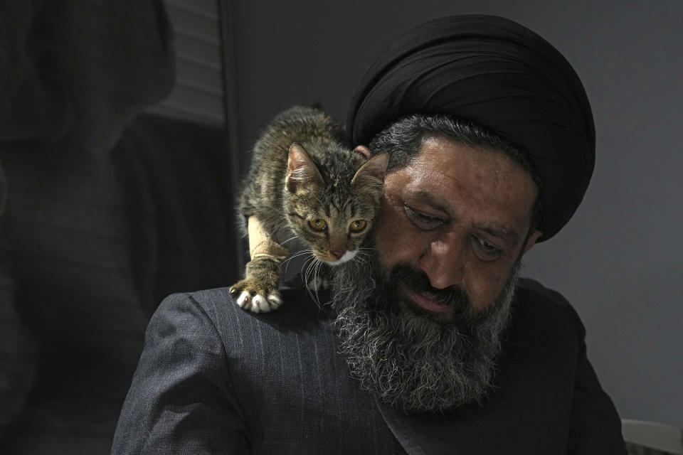 An injured stray cat walks on the shoulder of Iranian cleric Sayed Mahdi Tabatabaei after treatment at a veterinary clinic in Tehran, Iran, Friday, May 19, 2023. It's rare these days for a turbaned cleric in Iran to attract a large following of adoring young fans on Instagram, but Tabatabaei has done it by rescuing street dogs in defiance of a local taboo. (AP Photo/Vahid Salemi)