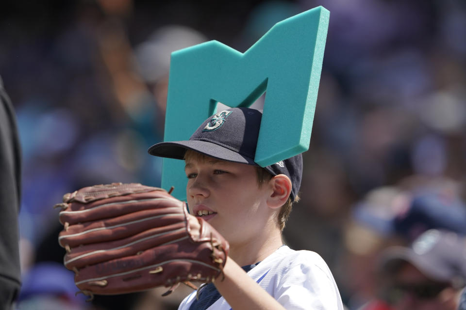 A young fan, wearing a vintage Seattle Mariners foam "M Head" and a glove, calls to players between innings of a baseball game between the Mariners and the Texas Rangers, Wednesday, July 27, 2022, in Seattle. (AP Photo/Ted S. Warren)