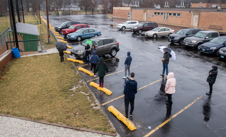 Peoria Notre Dame parishioners stand several feet apart as they wait their turn to use a confessional Thursday, March 19, in a baseball dugout behind the high school.