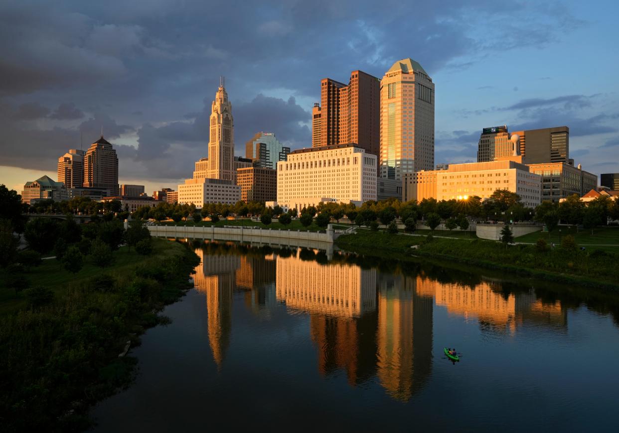 A man and a dog in a kayak take in a front-row view of the Downtown Columbus skyline as the sun sets in August over the Scioto Mile.