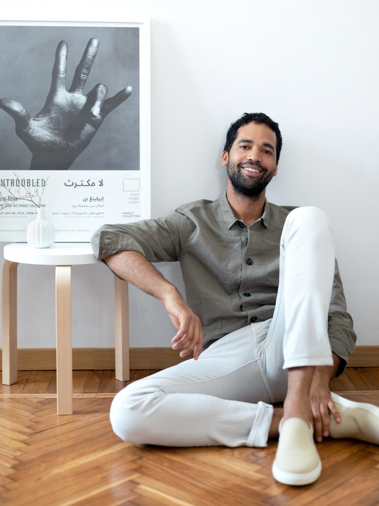 Alexandre-Camille Removille lounges in his Milan flat beside a white stool by Alvar Aalto, an Irving Penn poster from a 2019 exhibition in Beirut, and a vase by Richard Ginori from the Manifattura 1946 collection.