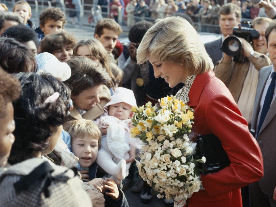 princess diana wearing red coat and holding flowers while meeting with admirers
