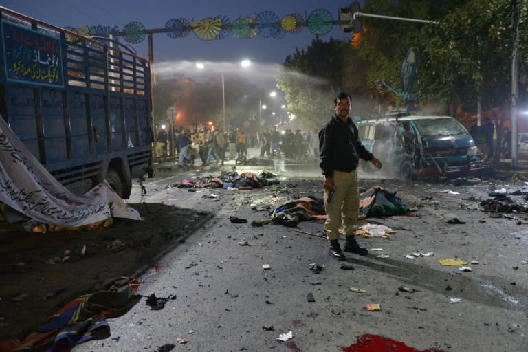 A Pakistani police officer stands alert beside the bodies of victims at the site after a powerful explosion in Lahore on February 13, 2017