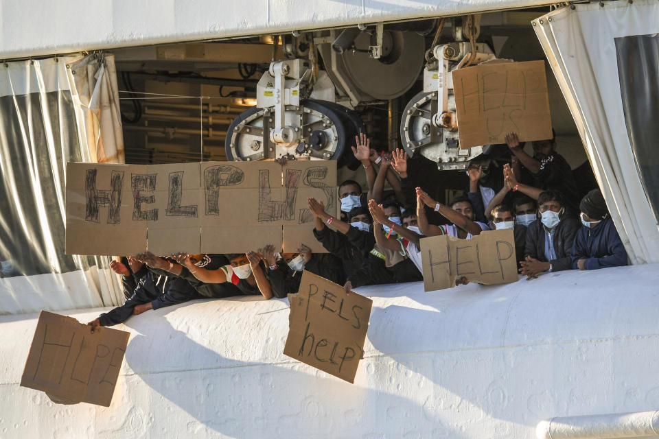 Migrants hold banners asking for help, from a deck of the Norway-flagged Geo Barents ship operated by Doctors Without Borders, in Catania's port, Sicily, southern Italy, Monday, Oct. 7, 2022. The Geo Barents has been allowed Sunday to disembark 357 migrant that Italian authorities defined as "vulnerable people" and minors, while leaving another 215 people that were declared non-vulnerable blocked on board. (AP Photo/Salvatore Cavalli)