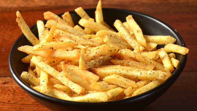 french fries with seasoning in black bowl on wooden table