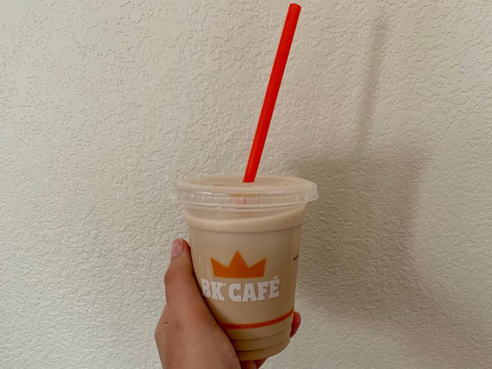 a hand holding a burger king iced coffee in front of a beige wall