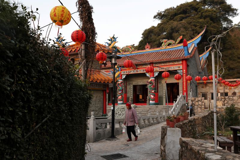 FILE PHOTO: Woman carrying water bottles walks past a temple at a village on Nangan island