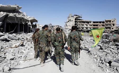 Fighters of Syrian Democratic Forces walk past the ruins of destroyed buildings near the National Hospital after Raqqa was liberated from the Islamic State militants, in Raqqa, Syria October 17, 2017. Picture taken October 17, 2017. REUTERS/Erik De Castro