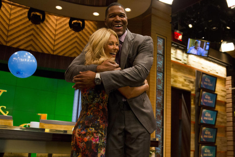 Former football player Michael Strahan, right, embraces Kelly Ripa on the set of the newly named "Live! with Kelly and Michael" on Tuesday, Sept. 4, 2012 in New York. Strahan joined the popular morning show as a permanent co-host on Tuesday, fulfilling a joking prophecy he made to Regis Philbin more than four years ago. The gap-toothed former New York Giant jogged onto the morning show set and picked up co-host Kelly Ripa in a bear hug, lifting her off her feet. He replaces Philbin, who left last November. Strahan was the survivor in a series of on-air tryouts of potential co-hosts since Philbin left, and his hiring has been an open secret for the past two weeks. (Photo by Charles Sykes/Invision/AP Images)